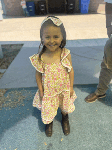 a little girl wearing a floral dress and brown boots smiles for the camera