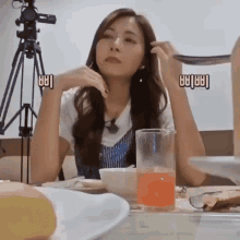 a woman is sitting at a table with a measuring cup in front of her and a camera in the background .
