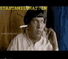 a man with a cigarette in his mouth is talking on a cell phone with the website starttamilchat.in written above him