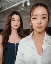 two women are standing next to each other and one is wearing a white shirt and the other is wearing a blue tank top