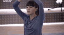 a woman in a blue shirt is stretching her arms in front of a microphone .