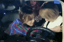 two women are sitting in a car and one is holding the steering wheel .