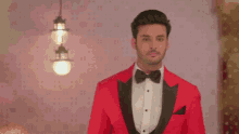 a man in a red tuxedo and bow tie stands in front of a pink wall