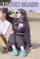 a girl is sitting on the grass with her hand on her head .