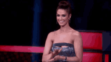 a woman in a strapless dress is sitting in a chair and clapping .