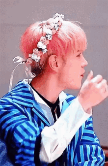 a man with pink hair and a flower crown on his head is wearing a blue jacket .