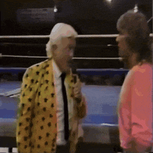 a man in a yellow jacket is holding a microphone and talking to another man