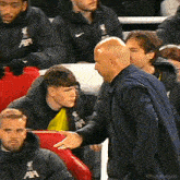 a man in a blue jacket is shaking hands with a young boy in a yellow shirt .