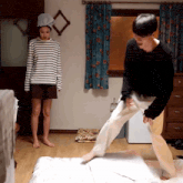 a woman in a striped shirt is standing next to a man who is standing on a pillow