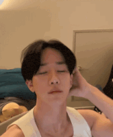 a young man in a white tank top is touching his hair