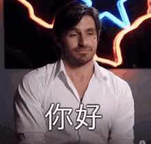 a man in a white shirt is sitting in front of a neon sign and making a funny face .
