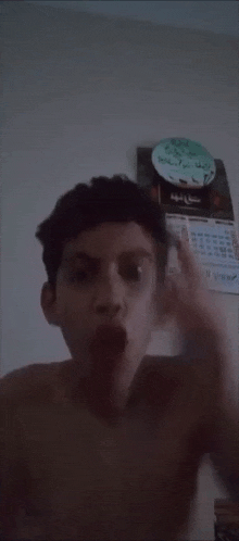 a shirtless young man making a funny face in front of a wall calendar