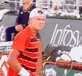 a man in a red striped shirt is holding a tennis racquet in front of an infosys sign