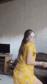 a woman in a yellow dress is dancing in front of a television in a living room .
