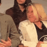 a woman in a white jacket is sitting next to a man in a suit and a woman in a black shirt .