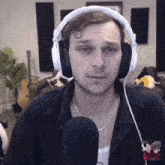 a man wearing headphones looks at the camera with a guitar in the background