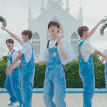 a group of young men in blue overalls are dancing in front of a white church