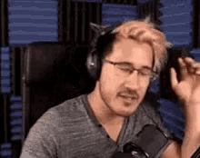 a man wearing headphones and glasses is sitting in front of a microphone in a recording studio .
