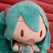 a stuffed toy of hatsune miku is sitting on a red couch with a surprised look on her face .