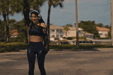 a woman wearing headphones and a black crop top is standing on a street