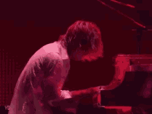 a man in a white shirt is playing a piano in a dark room with red lights .