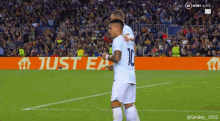 two soccer players are hugging on a field with an ad for just eat behind them