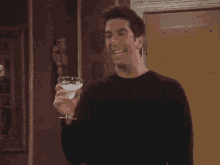 a man in a black sweater is holding a martini glass and laughing .