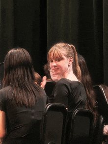 a girl in a ponytail sits in a row of black chairs