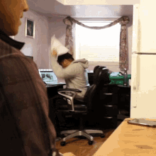 a man sitting in a chair holding a pillow in front of a laptop