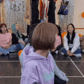 a girl wearing a purple hoodie with the letter d on it sits on the floor