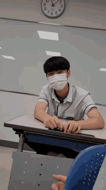 a boy wearing a face mask sits at a desk in front of a clock that shows the time as 7:15