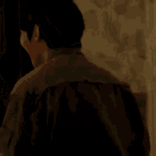 a man in a green jacket is standing in a dark room holding his fist in the air .