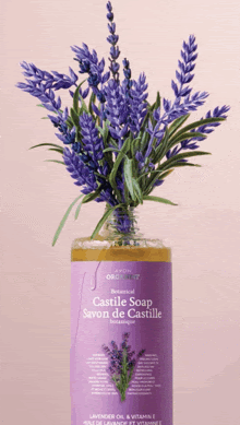 a bottle of castile soap with a bouquet of lavender flowers behind it