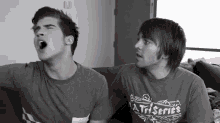 two men are sitting on a couch and one has a shirt that says a triseries