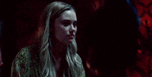 a woman with long blonde hair is standing in a dark room with a snake print shirt on .