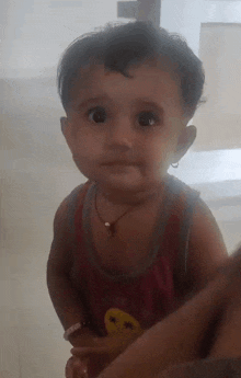 a baby in a red tank top with a smiley face on it