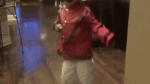 a young boy in a red jacket and white pants is walking down a hallway .