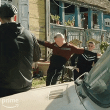 a man in a red sweater is standing next to a white car with the word prime on it