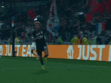 a soccer player is running on a field in front of a sign that says just eat