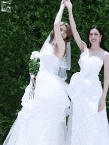 two women in white wedding dresses are holding hands and smiling .