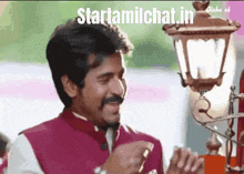a man with a mustache is smiling in front of a lamp with the words startamilchat.in written on the bottom
