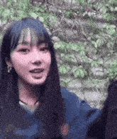 a woman with long black hair is standing in front of a tree and smiling .