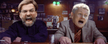 two men are sitting at a bar and one has a beard and one has glasses