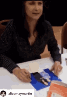 a woman is sitting at a table signing a picture with the name alicemaymartin in the corner