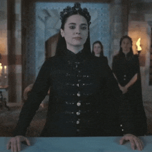 a woman in a black dress with a crown on her head stands in front of a group of women