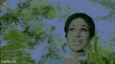 a woman in a blue saree is standing in a forest surrounded by trees and plants .