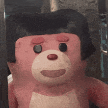 a pink teddy bear with a black wig on his head
