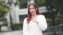 a woman in a white dress is holding her hand to her chest