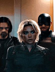 a woman in a black jacket is standing next to two men in a room .