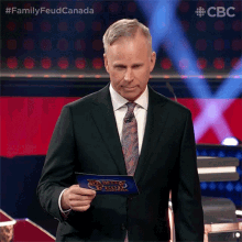 a man in a suit and tie is holding a piece of paper that says family feud canada on it